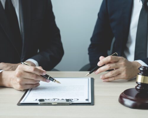 Lawyer hand holding pen and providing legal consult business dispute service to the man at the office with justice scale and gavel hammer.